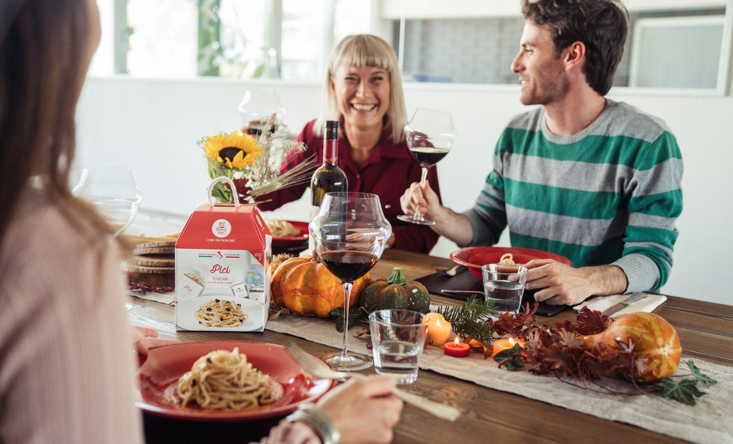 tavola imbandita in stile autunnale con persone che condividono felici un piatto di pasta e del vino